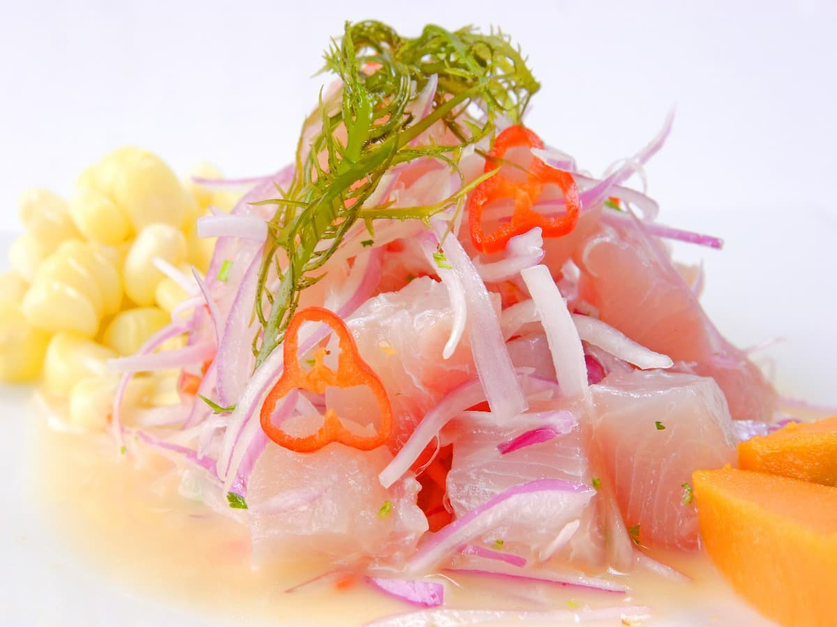cebiche de pescado con cebolla, chile, maíz dulce y decorado con algas frescas en restaurante en perú